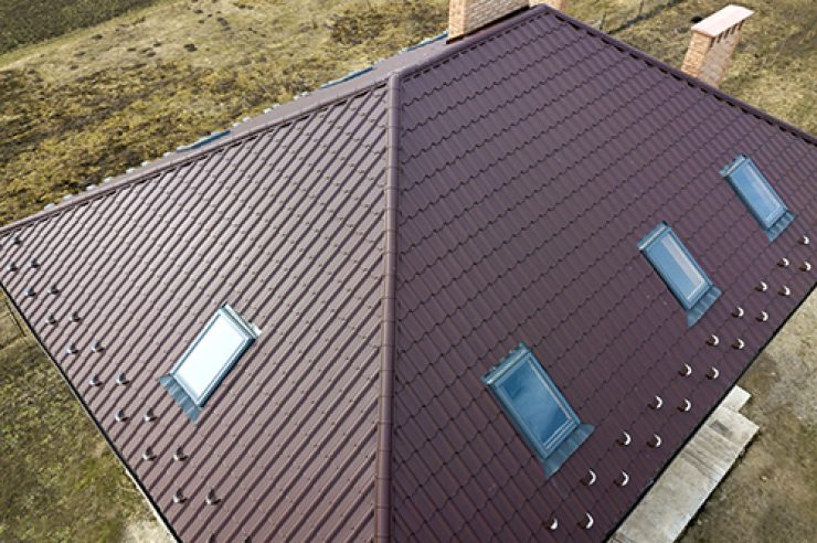 Aerial top view of building steep brown shingle roof, brick chimneys and small attic windows on house top with metal tile roof. Roofing, repair and renovation work.